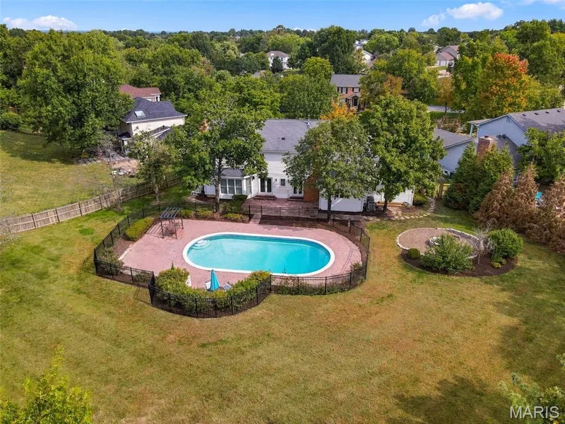 Expansive backyard featuring a fenced-in swimming pool with a brick paver surround, a circular paved patio, and mature trees — 2785 Sun Meadow Drive, Wildwood, MO 63005