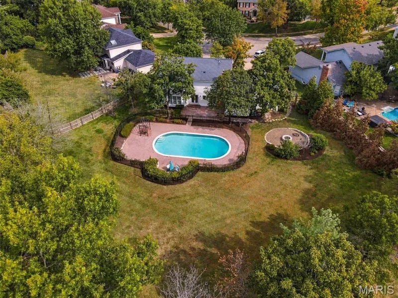 Oval-shaped swimming pool with a surrounding paver patio and black fencing — 2785 Sun Meadow Drive, Wildwood, MO 63005