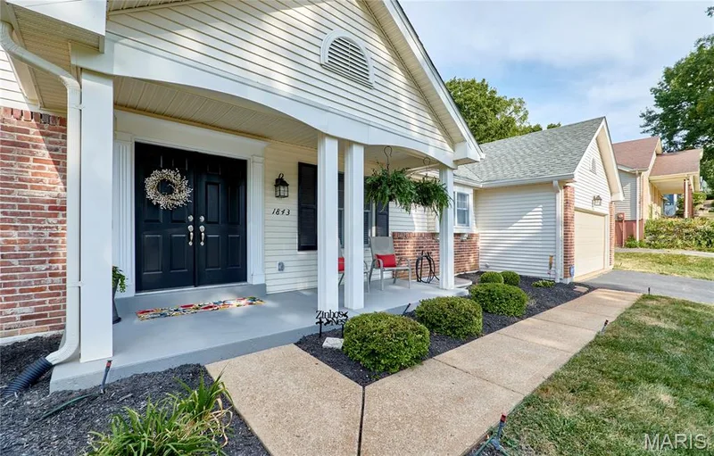 Covered front porch with white columns, dark double entry doors, exterior wall lantern, and brick accents — 1843 Shadywood Court, Chesterfield, MO 63017