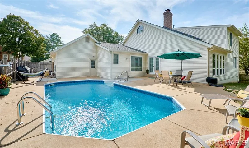 In-ground swimming pool, expansive concrete patio, white siding exterior, multiple windows, and a brick chimney — 1843 Shadywood Court, Chesterfield, MO 63017