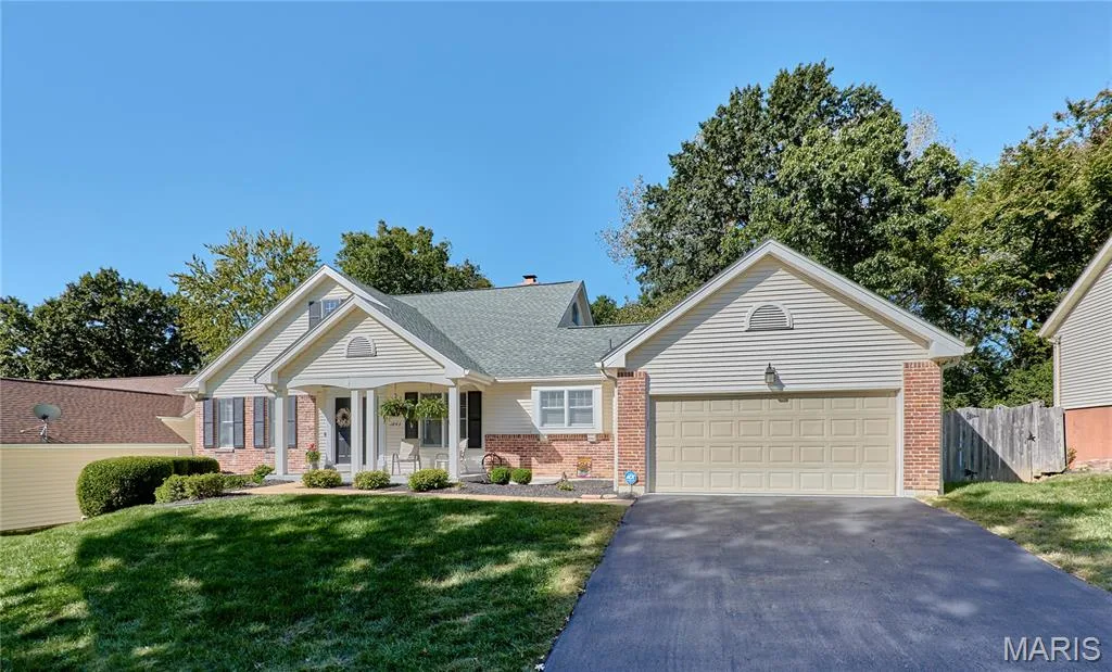 Exterior featuring brick and siding finishes, a covered front entry with columns, an attached garage, a paved driveway, and established landscaping — 1843 Shadywood Court, Chesterfield, MO 63017