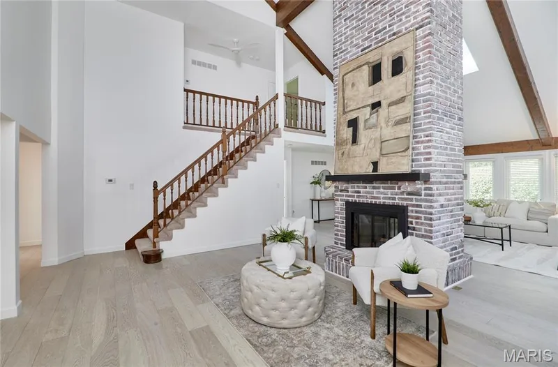 Two-story brick fireplace with a wood mantle, light wood-finish flooring, and exposed ceiling beams — 1843 Shadywood Court, Chesterfield, MO 63017