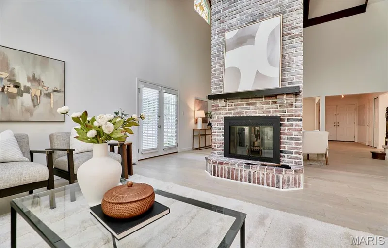 Vaulted ceiling living area featuring a brick fireplace with mantel, double French doors, and light wood-finish flooring — 1843 Shadywood Court, Chesterfield, MO 63017