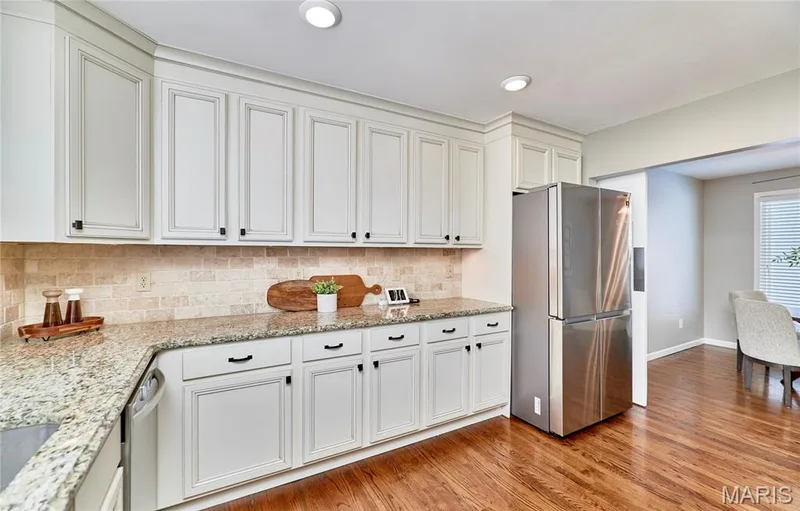 White shaker-style cabinetry, stainless steel refrigerator, granite countertops, tile backsplash, and wood-finish flooring — 1843 Shadywood Court, Chesterfield, MO 63017
