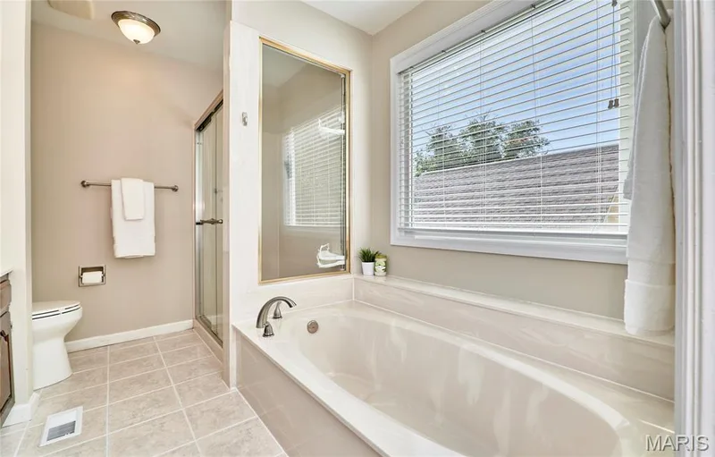 Built-in soaking tub, separate glass-enclosed shower, window with blinds, and tiled flooring — 1843 Shadywood Court, Chesterfield, MO 63017