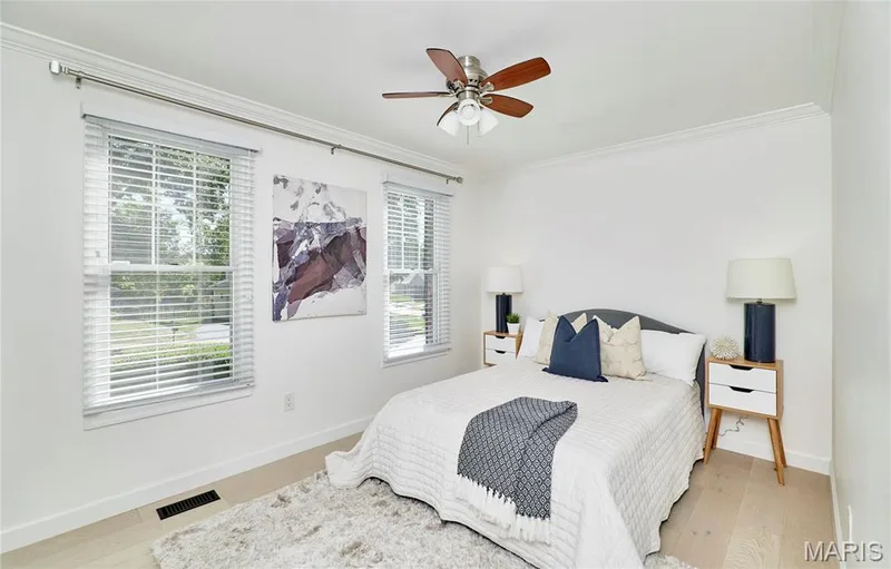Light wood-finish flooring, dual windows with blinds, ceiling fan with integrated lighting, crown molding, and white wall finishes — 1843 Shadywood Court, Chesterfield, MO 63017