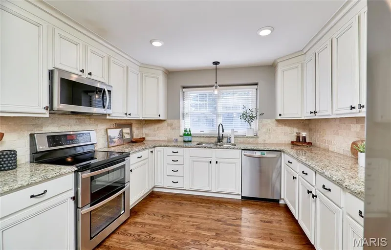 Kitchen featuring wood-finish flooring, white cabinetry, stainless steel appliances, speckled countertops, and a tile backsplash — 1843 Shadywood Court, Chesterfield, MO 63017