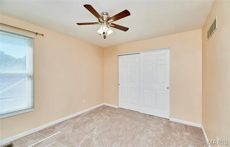 Upper level bedroom with window with blinds, a ceiling fan with integrated lighting, paneled bi-fold closet doors, and carpeted flooring — 1843 Shadywood Court, Chesterfield, MO 63017