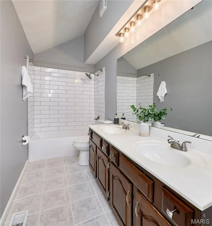 Upper level full bath with vaulted ceiling with an integrated light fixture, dual vanity with dark wood-finish cabinetry, white countertop, large wall-mounted mirror, and a shower/tub combination with white subway tile — 1843 Shadywood Court, Chesterfield, MO 63017