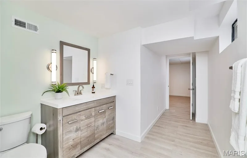 Bathroom featuring a vanity with a wood-finish cabinet, a rectangular mirror, and dual wall-mounted sconces — 1843 Shadywood Court, Chesterfield, MO 63017