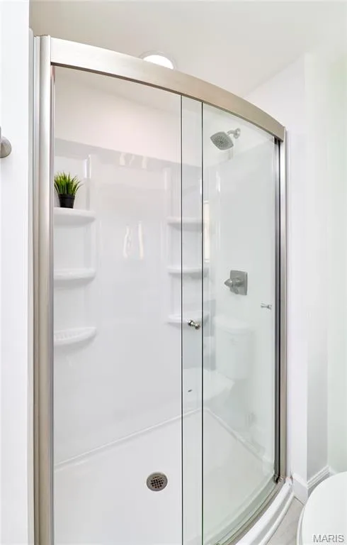Curved glass shower enclosure with brushed nickel framing, integrated shelving, and a showerhead with coordinating fixtures — 1843 Shadywood Court, Chesterfield, MO 63017