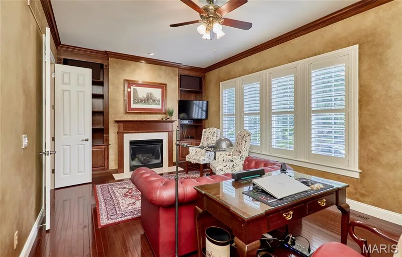 Warm-toned walls with elegant wood trim, a built-in fireplace, rich wood-finish flooring, and white plantation shutters — 1970 Chesterfield Ridge Circle, Chesterfield, MO 63017