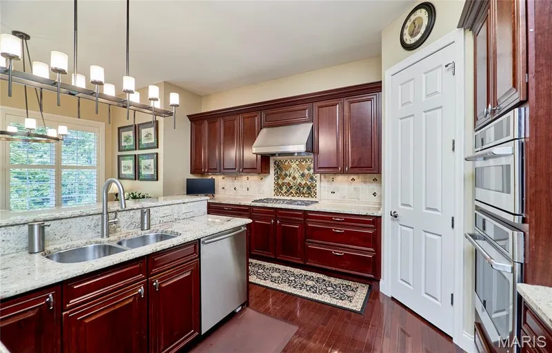 Kitchen featuring rich wood cabinetry, stainless steel appliances, granite countertops, a double basin sink, and wood-finish flooring — 1970 Chesterfield Ridge Circle, Chesterfield, MO 63017