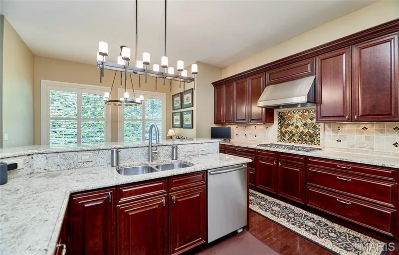 Granite countertops, dark wood-finish cabinetry, stainless steel appliances, tile backsplash, and a contemporary linear chandelier — 1970 Chesterfield Ridge Circle, Chesterfield, MO 63017