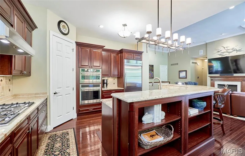 Chef's kitchen featuring rich wood cabinetry, stainless steel built-in appliances including, granite countertops, a spacious center island with open shelving, and hardwood flooring throughout — 1970 Chesterfield Ridge Circle, Chesterfield, MO 63017