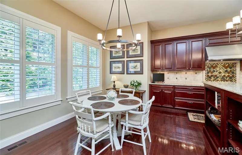 Hardwood-finish flooring, white plantation shutters, dark wood-finish cabinetry, light-toned backsplash tiling, and stone countertops — 1970 Chesterfield Ridge Circle, Chesterfield, MO 63017