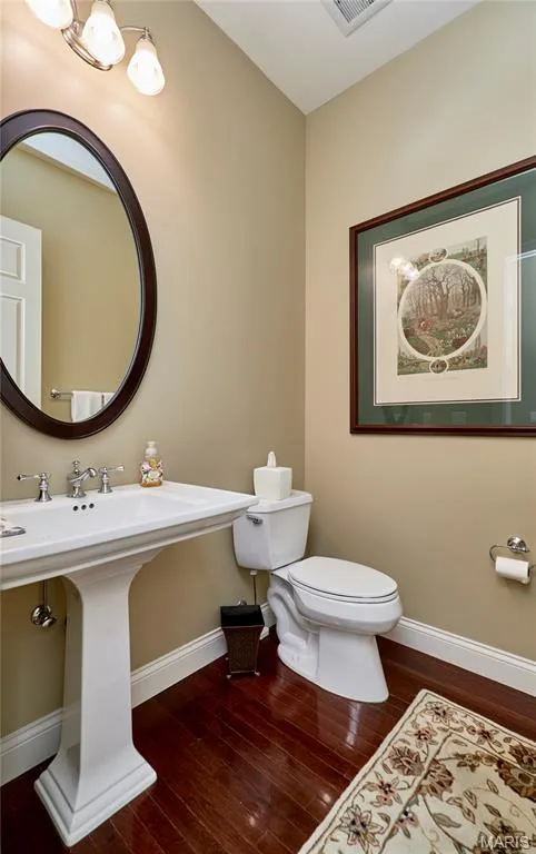 Pedestal sink with chrome fixtures, oval mirror, wall-mounted light fixture, and wood-finish flooring — 1970 Chesterfield Ridge Circle, Chesterfield, MO 63017