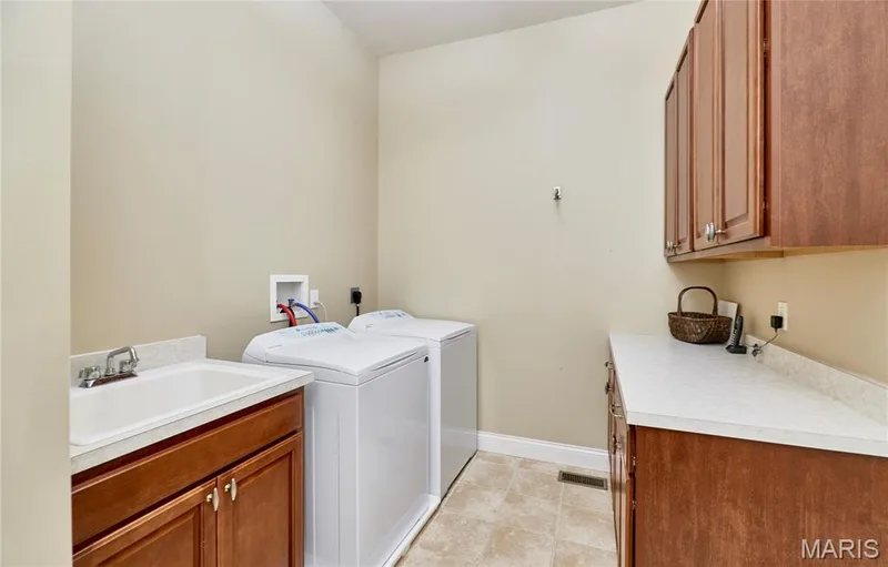 Laundry area featuring a utility sink with a chrome faucet, wood-finish cabinetry, and a light-toned countertop — 1970 Chesterfield Ridge Circle, Chesterfield, MO 63017