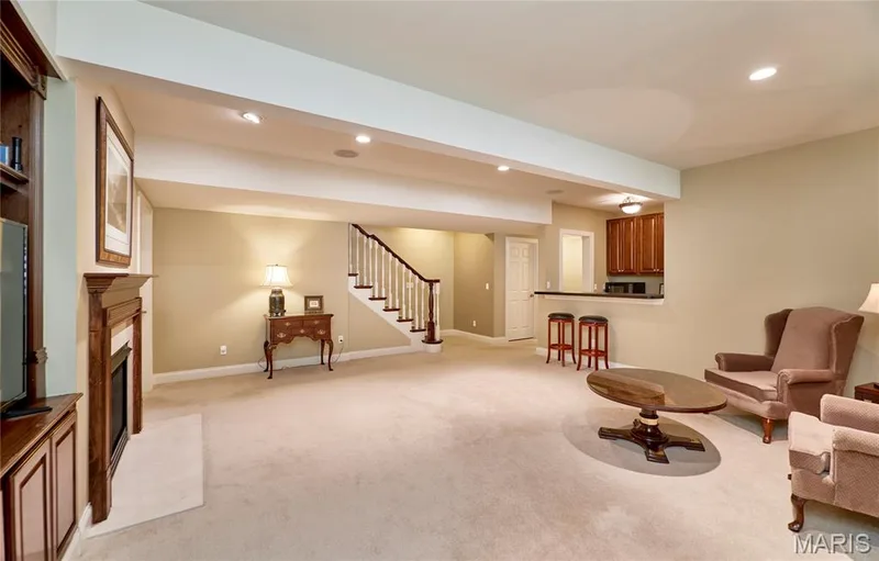 Spacious lower level featuring recessed lighting, a built-in fireplace with wood mantel, carpet flooring, a wood staircase with white balusters, and a wet bar with wood cabinetry — 1970 Chesterfield Ridge Circle, Chesterfield, MO 63017