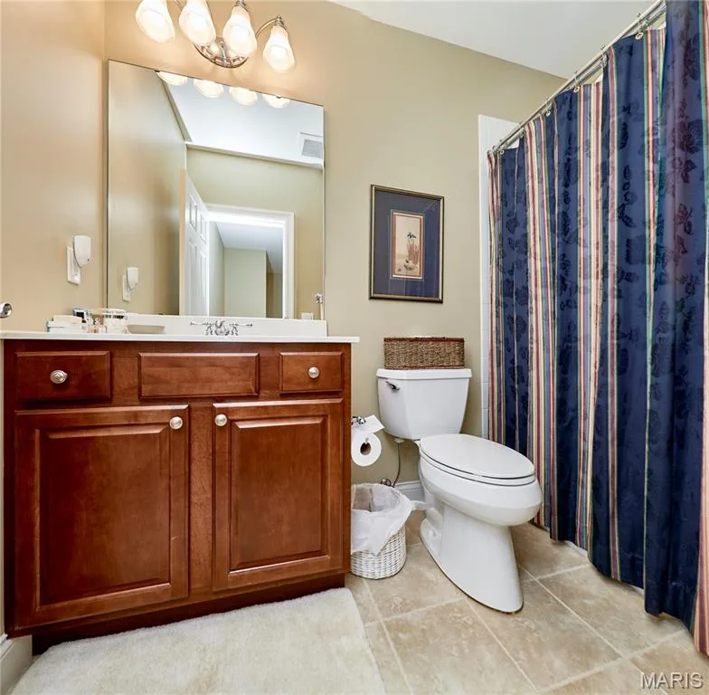 Bathroom featuring a wood-finish vanity with a white countertop, a large wall-mounted mirror, a four-light fixture, and ceramic tile flooring — 1970 Chesterfield Ridge Circle, Chesterfield, MO 63017