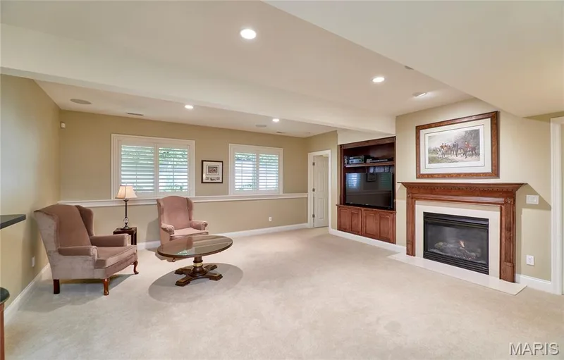 Recessed lighting, wood-finish built-in media cabinet, fireplace with wood-finish mantel and stone surround, two windows with louvered shutters, and light-tone carpeting — 1970 Chesterfield Ridge Circle, Chesterfield, MO 63017