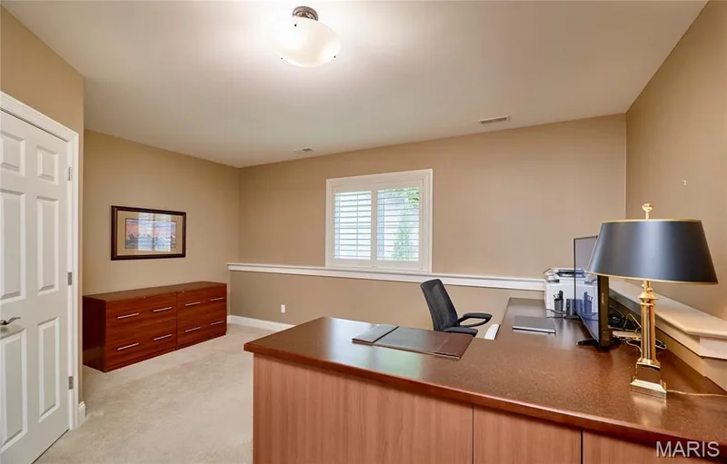 Carpeted room featuring a white paneled door, built-in desk, built-in storage cabinetry, white plantation shutters, and a semi-flush mount ceiling light fixture — 1970 Chesterfield Ridge Circle, Chesterfield, MO 63017