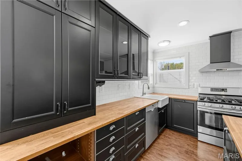 Glass door upper cabinets, a stainless steel range with hood, and a farmhouse sink — 242 Ashford Oaks Drive, Wentzville, MO 63385