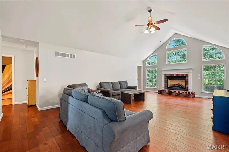 Vaulted ceiling featuring a ceiling fan, wood-finish flooring, brick-surround fireplace with a white mantel, and arched windows — 521 Sceptre Road, Wentzville, MO 63385
