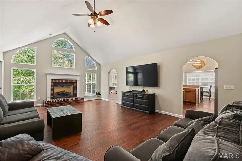 Vaulted ceiling with a ceiling fan, wood-finish flooring, brick-surround fireplace with a mantel, arched window features, and arched doorways — 521 Sceptre Road, Wentzville, MO 63385