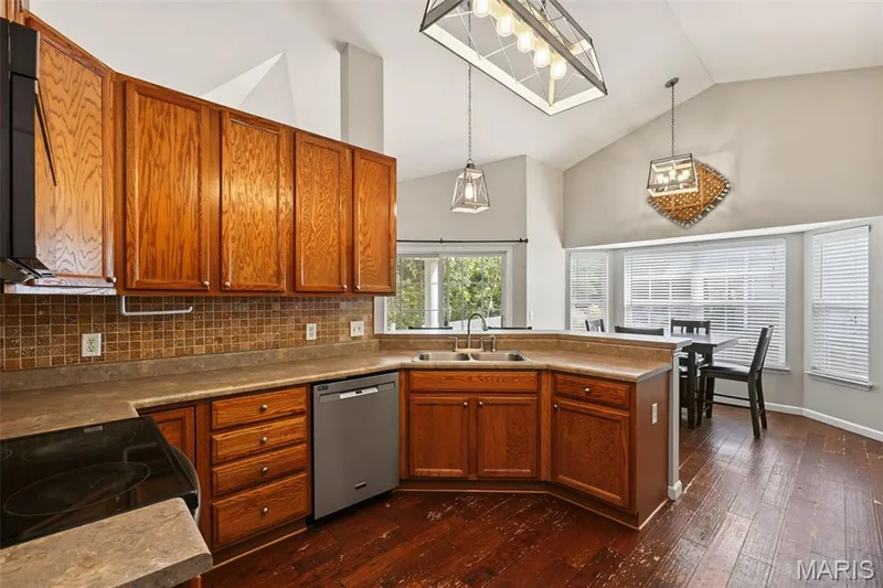 Vaulted ceiling kitchen with wood-finish flooring, ample wood cabinetry, and a stainless steel dishwasher — 521 Sceptre Road, Wentzville, MO 63385