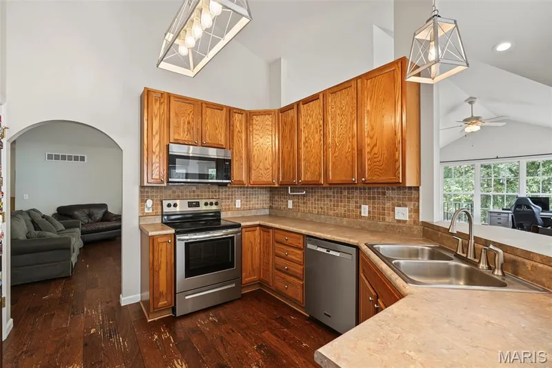Kitchen featuring wood-finish cabinetry, stainless steel appliances, a tile backsplash, and a double basin sink — 521 Sceptre Road, Wentzville, MO 63385