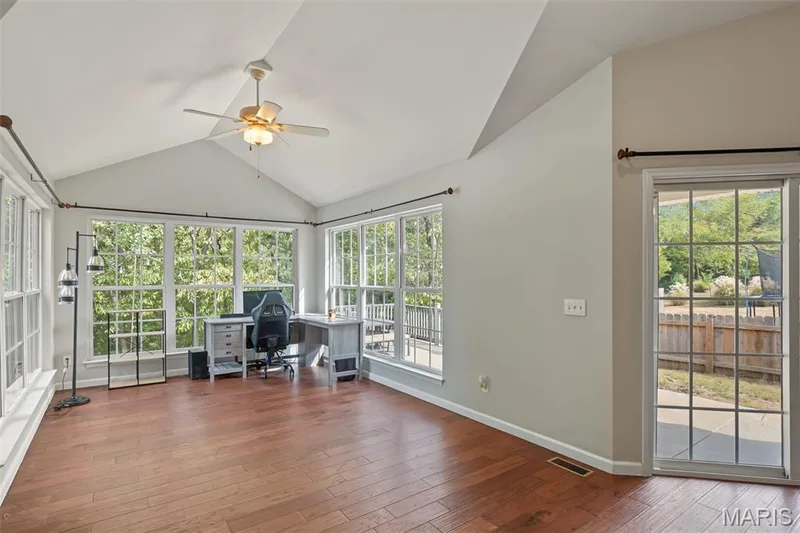 Vaulted ceiling with a ceiling fan, wood-finish flooring, numerous windows with grid patterns, and a sliding glass door leading to the exterior — 521 Sceptre Road, Wentzville, MO 63385