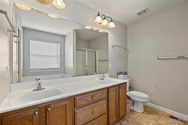 Dual vanity with wood-finish cabinetry, a large wall-mounted mirror, and a three-light fixture — 521 Sceptre Road, Wentzville, MO 63385