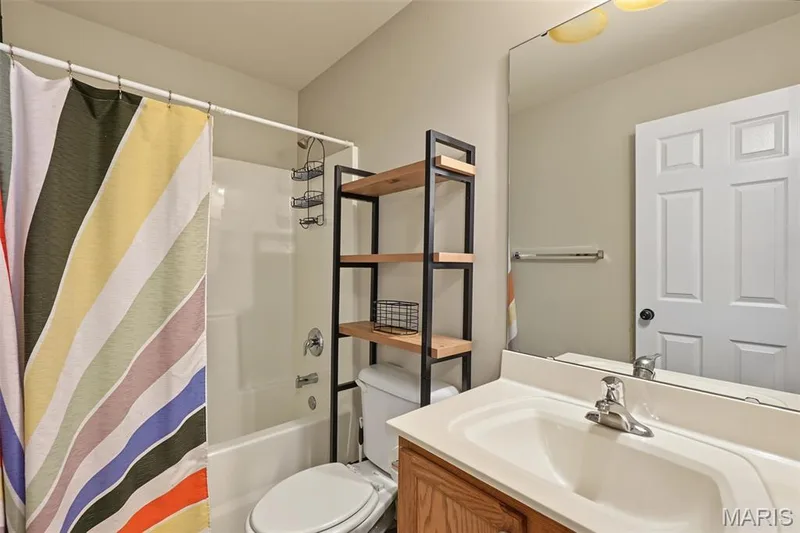 White bathtub with an integrated shower, single vanity with a white countertop, and a built-in mirror — 521 Sceptre Road, Wentzville, MO 63385