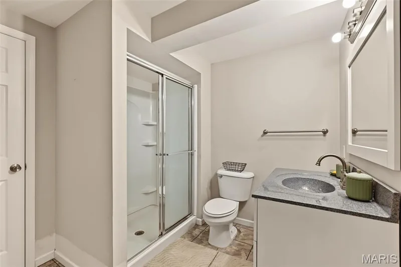 Walk-in shower with sliding glass doors, single vanity with a dark stone countertop, undermount sink, and brushed nickel faucet — 521 Sceptre Road, Wentzville, MO 63385