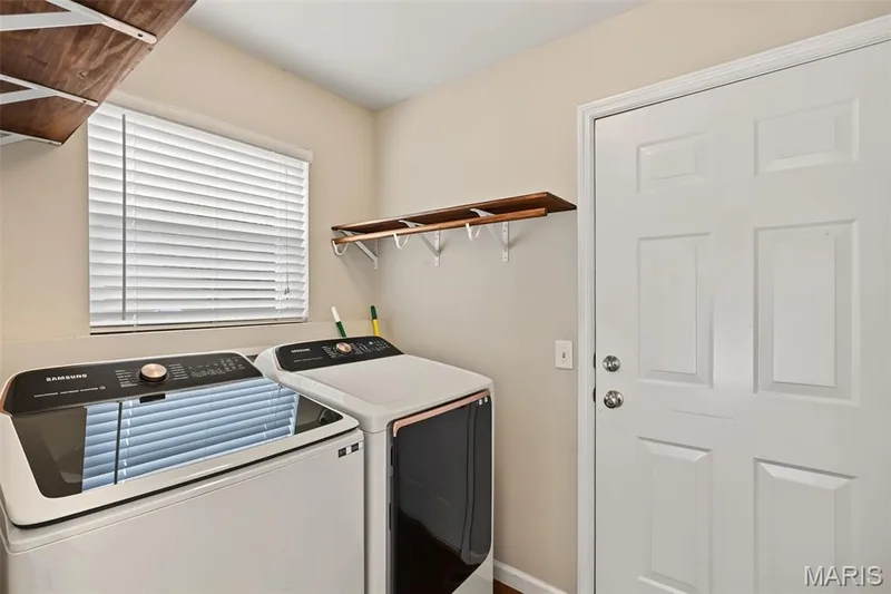 Laundry area featuring a window with horizontal blinds and a wooden shelf with hanging hooks — 521 Sceptre Road, Wentzville, MO 63385