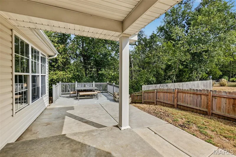 Covered concrete patio with a raised deck, wood privacy fence, and multiple windows — 521 Sceptre Road, Wentzville, MO 63385