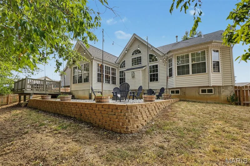 Exterior featuring light-toned siding, a multi-level deck, a stone block retaining wall, a patio area, and multiple windows — 521 Sceptre Road, Wentzville, MO 63385