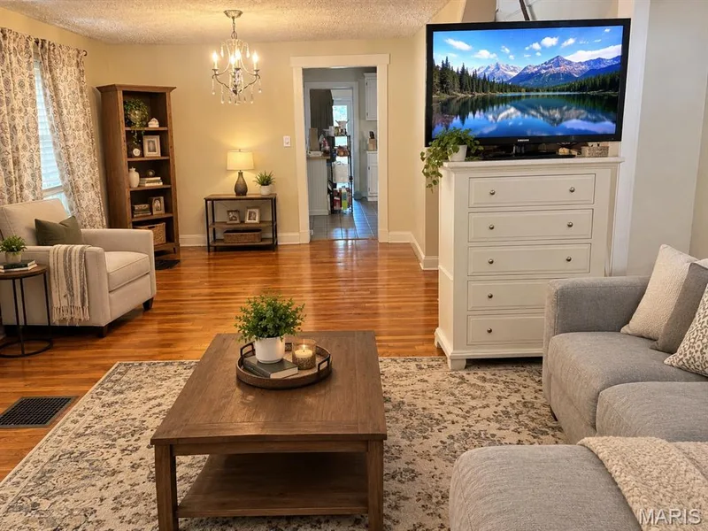 Living area featuring polished wood-finish flooring, a multi-arm crystal chandelier, and a doorway with a decorative surround — 411 Adams Street, St Charles, MO 63301