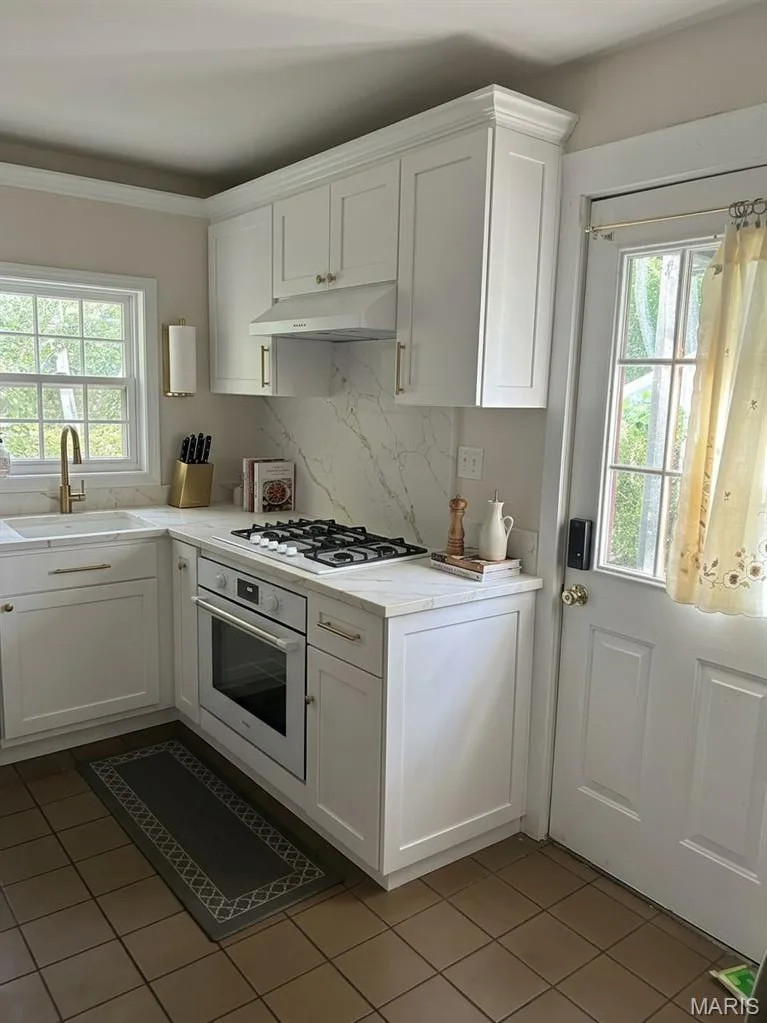 Kitchen featuring white shaker-style cabinetry, stone-patterned countertops, a gas cooktop, built-in oven, and a brass-finish faucet — 411 Adams Street, St Charles, MO 63301