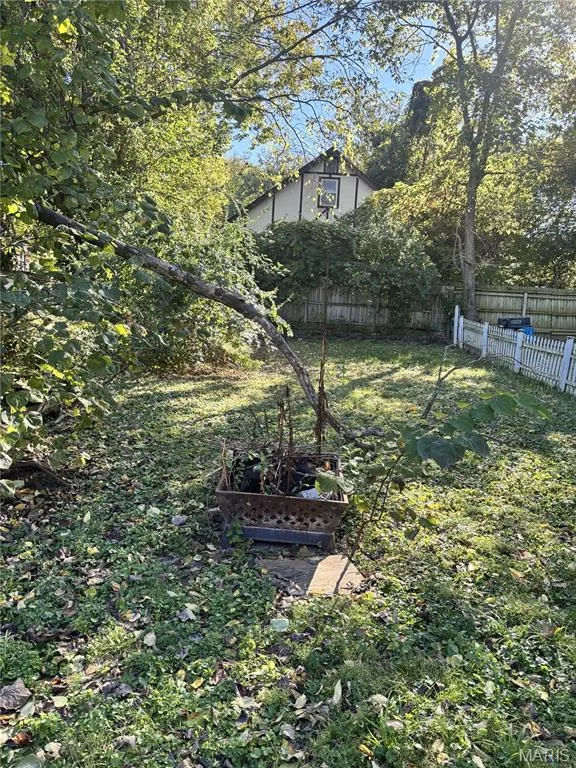 Backyard featuring mature trees, a white picket fence, and a wood-panel privacy fence — 411 Adams Street, St Charles, MO 63301