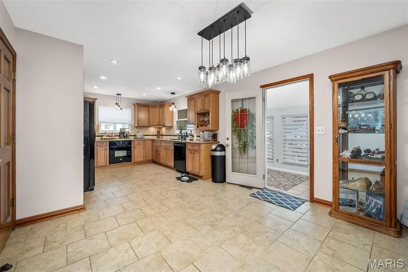 Kitchen featuring wood-finish cabinetry, black appliances, tile flooring, and a multi-light chandelier — 355 Birmingham Drive, O'Fallon, MO 63366