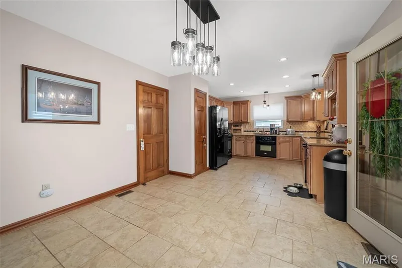 Spacious kitchen featuring warm wood cabinetry, neutral tile flooring, black appliances, and recessed lighting — 355 Birmingham Drive, O'Fallon, MO 63366
