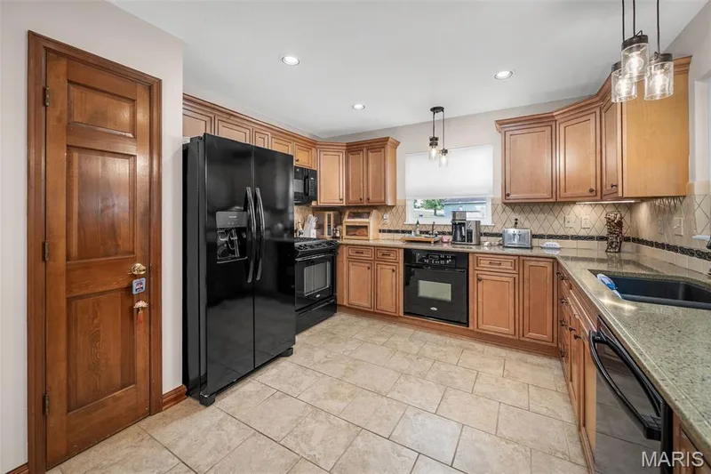 Kitchen featuring wood cabinetry, stone countertops, black appliances, tile flooring, and a tiled backsplash — 355 Birmingham Drive, O'Fallon, MO 63366