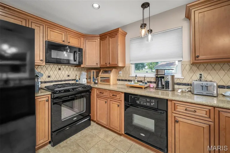 Kitchen featuring wood cabinetry, black appliances, tile flooring, and a decorative tile backsplash — 355 Birmingham Drive, O'Fallon, MO 63366