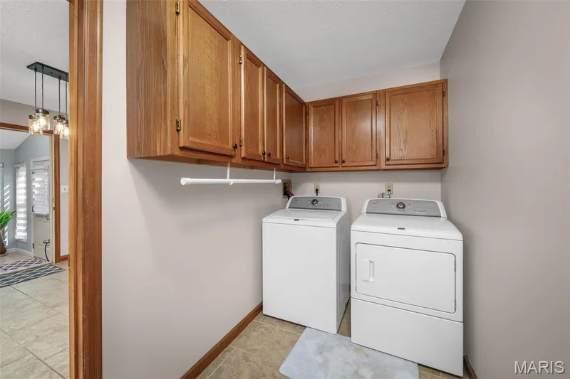 Integrated laundry area featuring wood-finish cabinetry, a built-in hanging rod, and tile flooring — 355 Birmingham Drive, O'Fallon, MO 63366