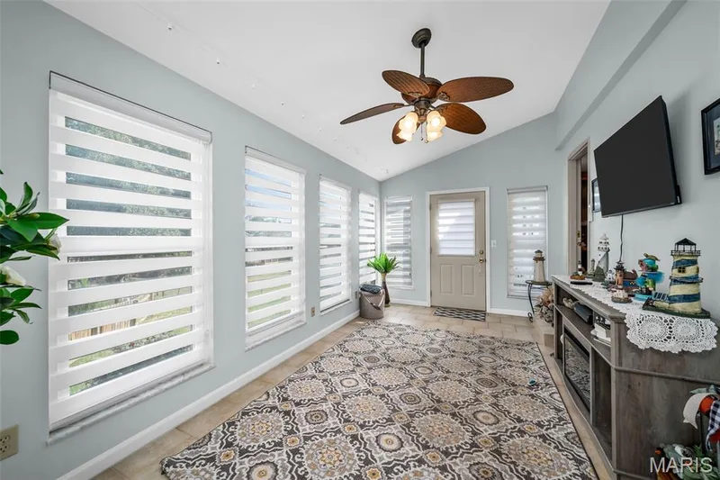 Vaulted ceiling, ceiling fan with integrated lighting, multiple windows with blinds, ceramic tile flooring, and a mounted television — 355 Birmingham Drive, O'Fallon, MO 63366