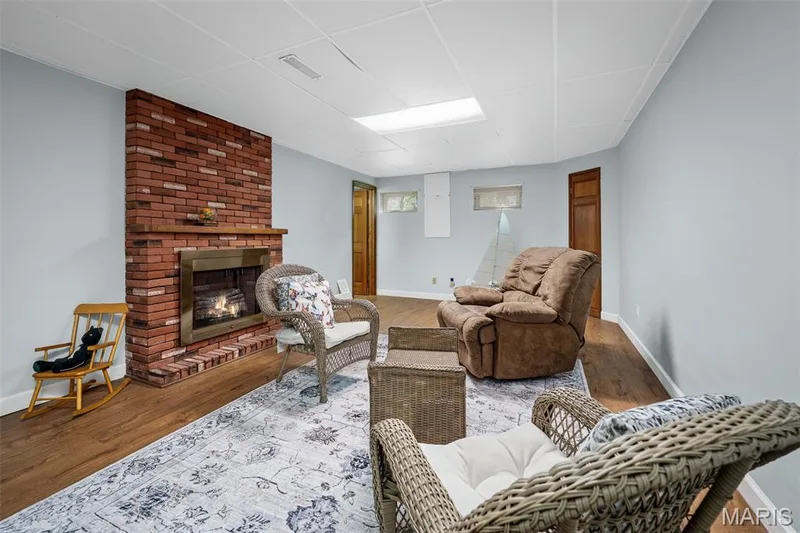 Brick fireplace with metal insert, wood-finish flooring, light blue painted walls, drop ceiling, and wood interior doors — 355 Birmingham Drive, O'Fallon, MO 63366