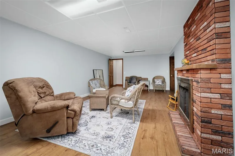 Spacious interior featuring wood-finish flooring, a brick fireplace with a wood mantle, and light-toned walls — 355 Birmingham Drive, O'Fallon, MO 63366