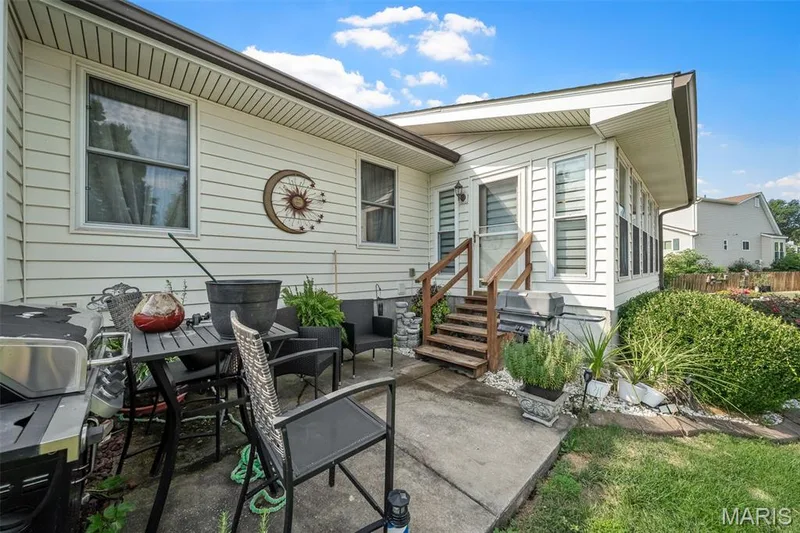 Exterior patio with concrete surface, white horizontal siding, and natural wood steps leading to an enclosed sunroom — 355 Birmingham Drive, O'Fallon, MO 63366